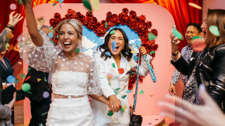 Two women walk through confetti after getting married.