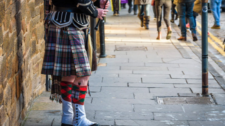 A man wearing a kilt plays the bagpipes. 