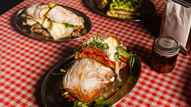 Plates of assorted panini-style sandwiches on a red and white checkered tablecloth.