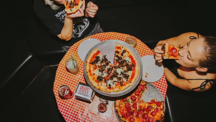 Two women eating slices of pizza at a table. 