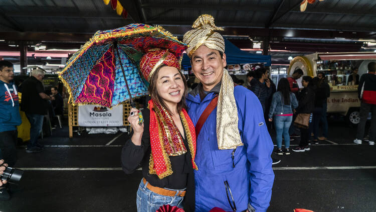 Two people wearing traditional Indian clothing, one is holding a parasol. 