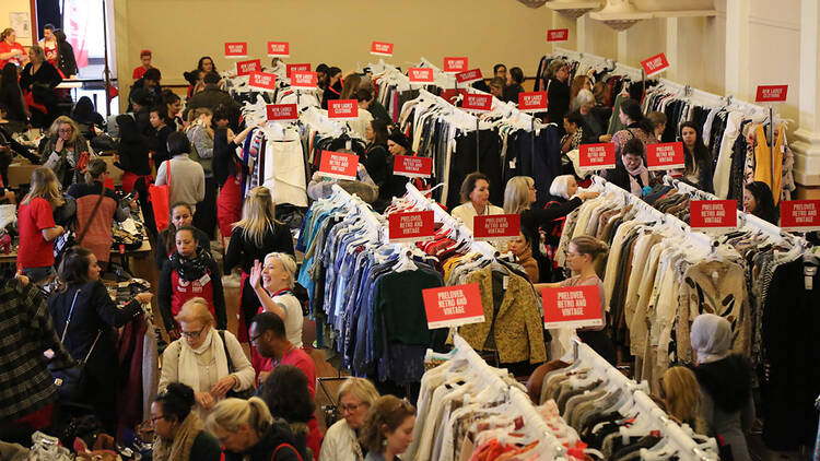 Shoppers walk between racks of clothing. 