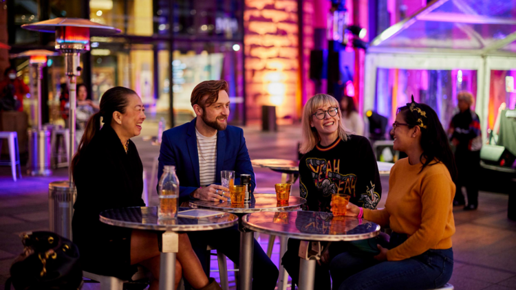 Four people at an outdoor bar having cocktails