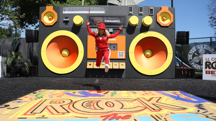 A woman jumps in front of a large depiction of a boombox.