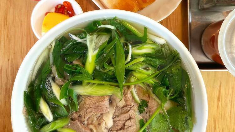 Bowl of beef pho with savoury doughnuts and a can of sugar-free Coke.