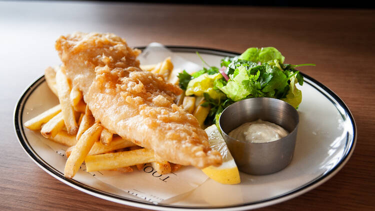 Fish, chips, salad and a white sauce with a wedge of lemon.