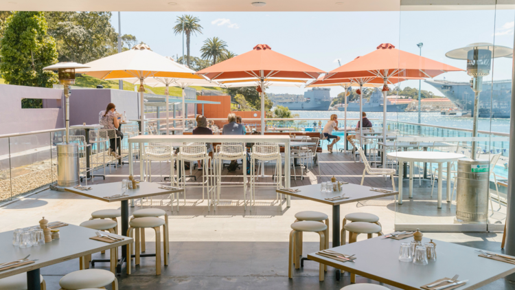 A deck with dining seating overlooking a Harbour pool