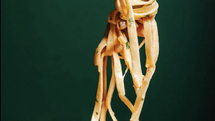A fork twirling pasta in a bowl in front of a green background. 