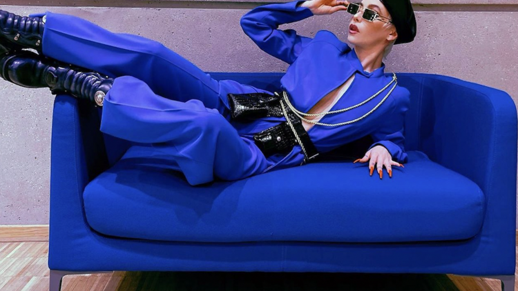A model in a blue jumpsuit poses on a blue couch.