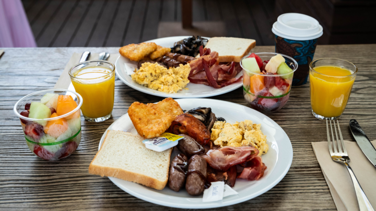 Two plates with a hot breakfast, plus fresh fruit and coffee on the side 