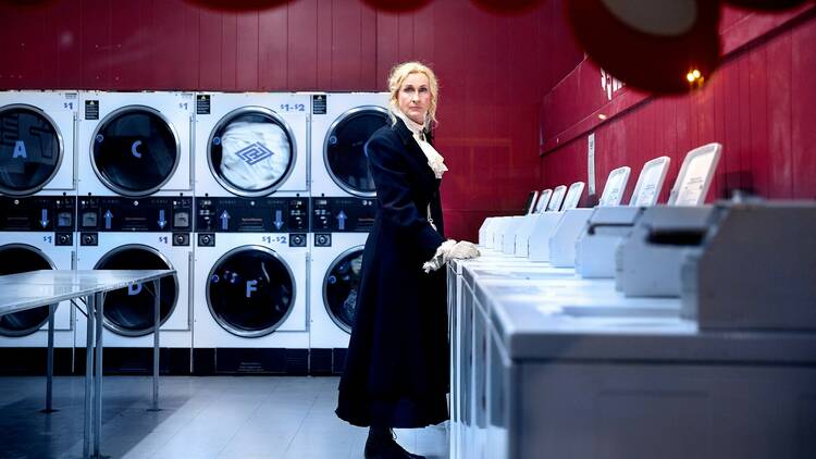 A woman stands at a laundromat looking at the camera