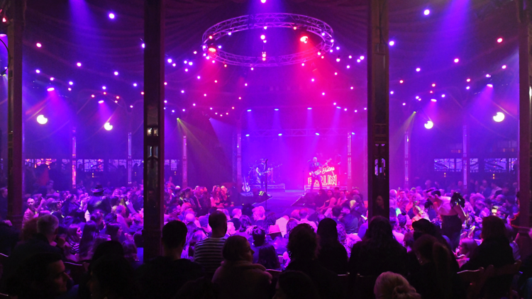 A crowded room and a stage with neon pink and purple lights