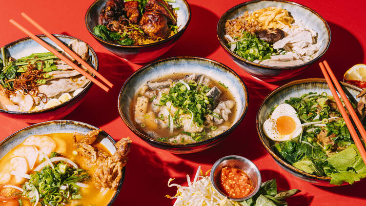 Assorted bowls of Asian soup and chopsticks on a red background. 