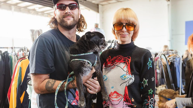 Two people wearing sunglasses and holding a dog. 