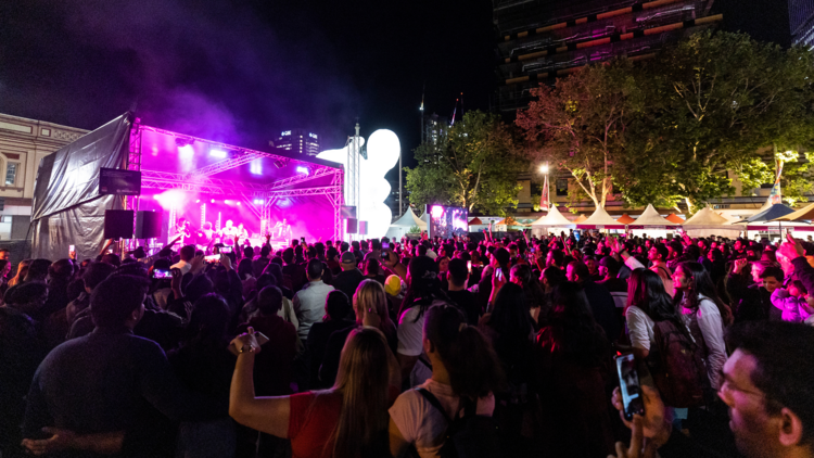 A festival with a big crowd in front of a pink neon stage