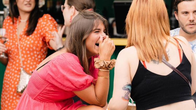 Woman in bright pink dress laughing with friends in Welcome to Thornbury's beer garden.