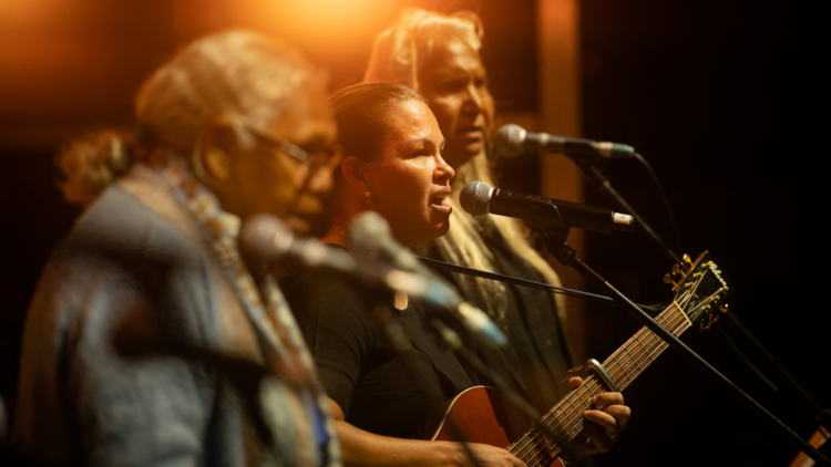 Three Indigenous singers on stage in front of microphones