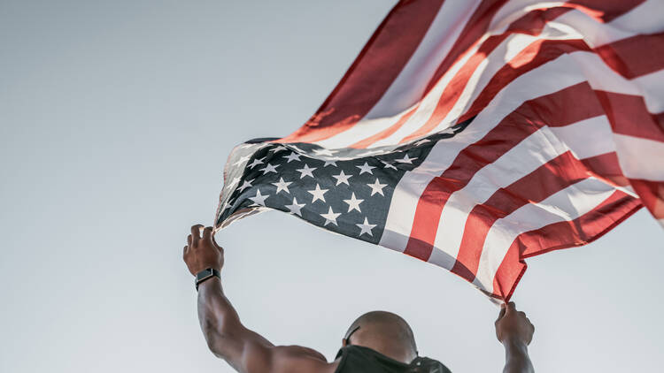 Low angle view of an athlete running on athletic track holding the American flag over the head