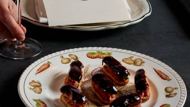 Choux pastries on a decorated plate and a glass of red wine on a table with menus and napkins.