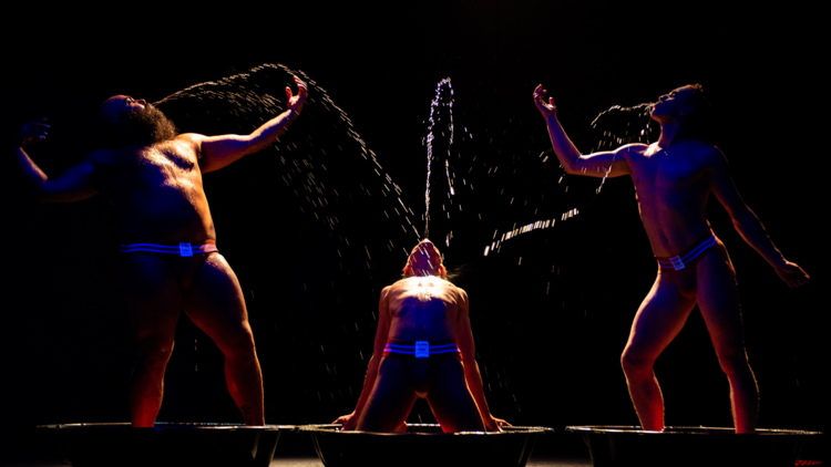 Three circus performers in the dark spitting water
