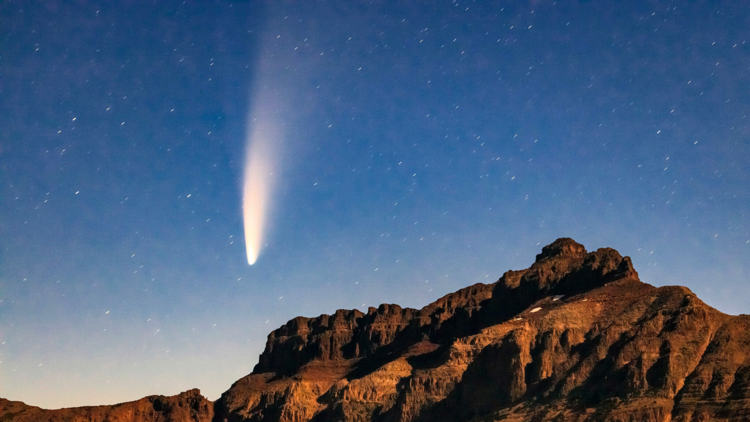 A bright white comet over a mountain peak 