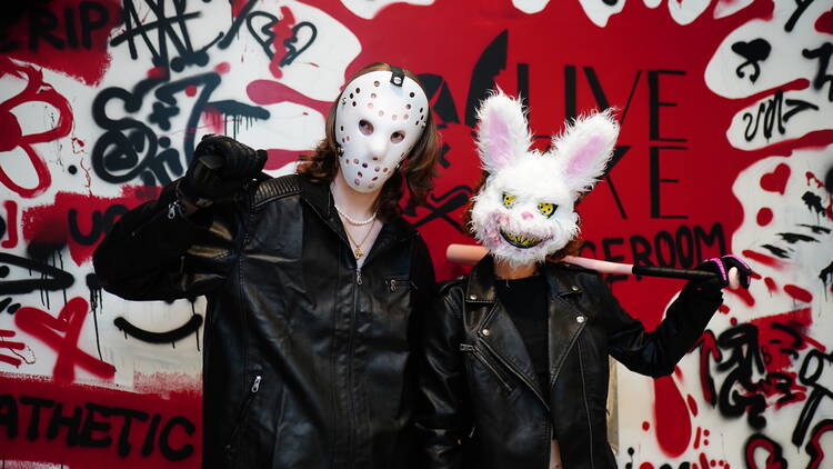 Two people in leather jackets and masks at a rage room.