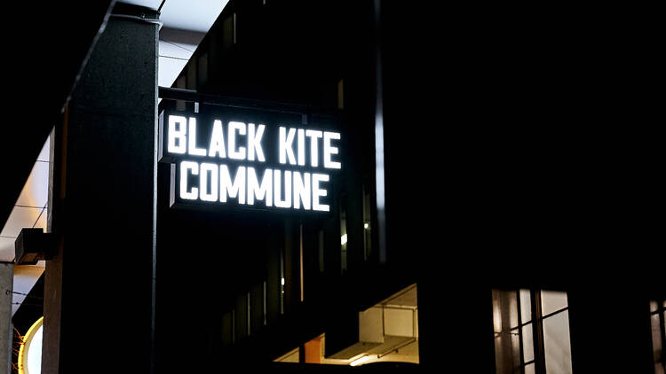 Neon-lit Black Kite Commune sign.
