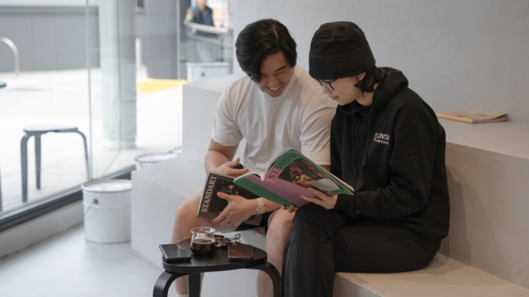 Two people sitting on the bench with coffees and reading a magazine