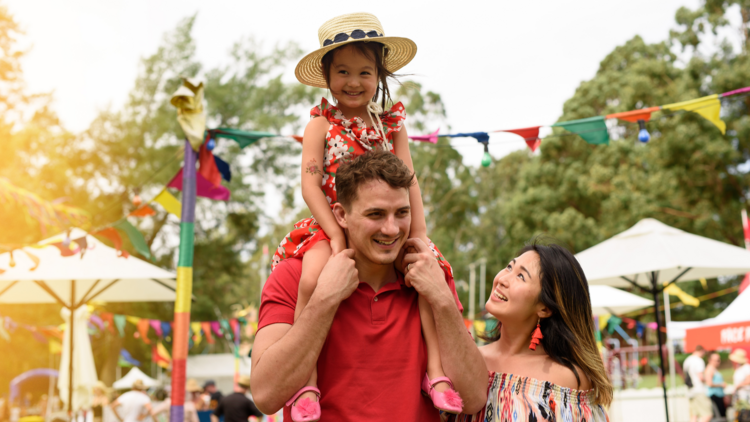 A kid siting on her dad's shoulders at a fair