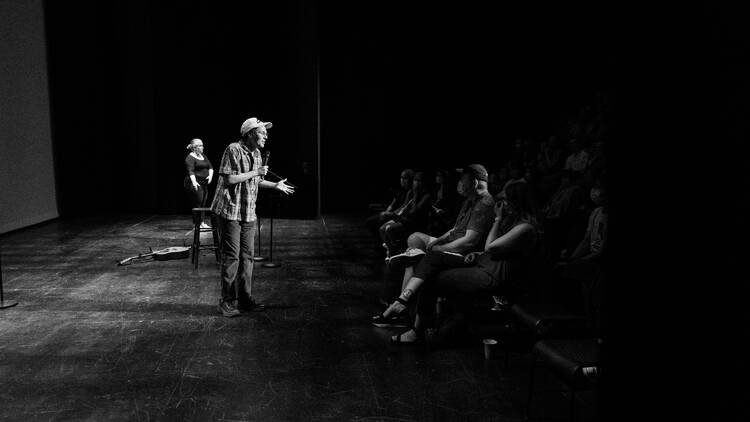 A comedian talks to an audience in a black-and-white photo.