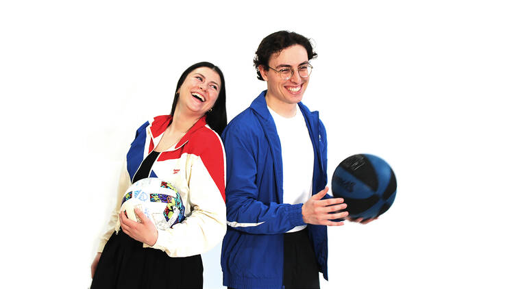 A man and woman holding soccer balls and basketballs.