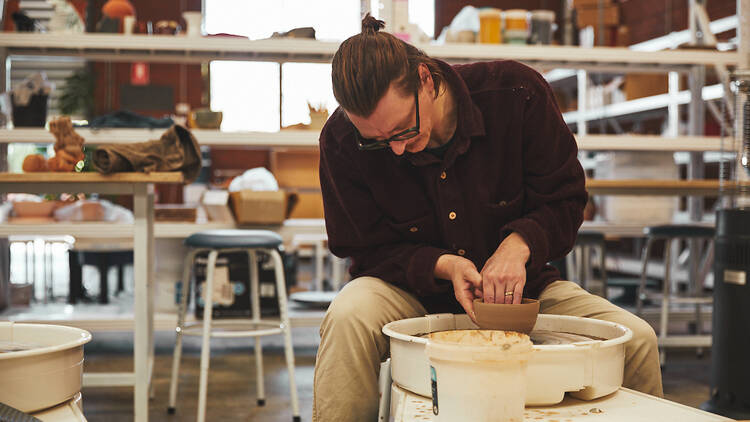 A man sitting at a pottery wheel spinning a bowl. 