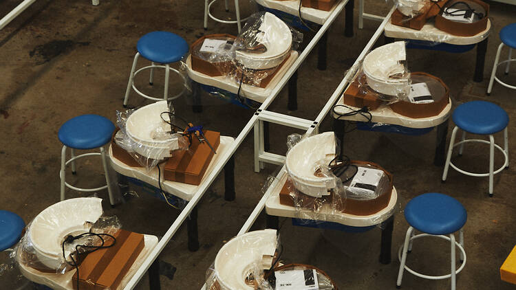 Rows of pottery wheels with stools next to them. 