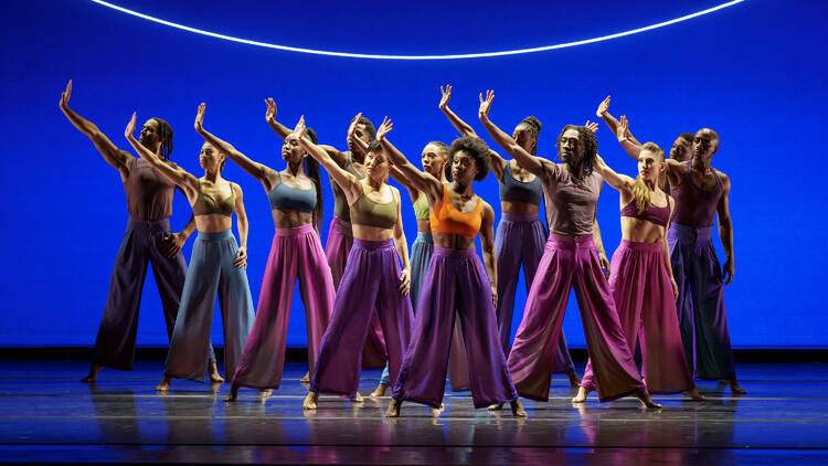 12 dancers of Alvin Ailey American Dance Theater standing on stage in front of a blue backdrop
