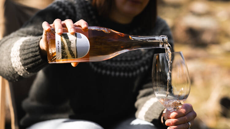 Woman pouring rose wine into a glass outdoors.