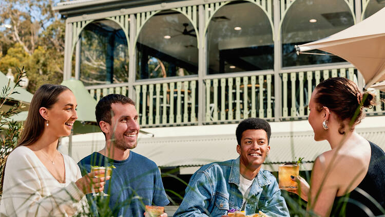 Four diners sitting with drinks and foods in an outdoor dining area at Studley Park Boathouse.