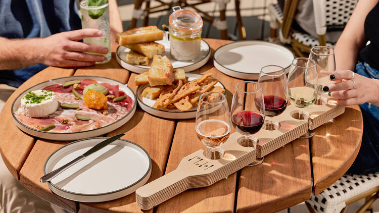 A wooden table featuring a tasting paddle of glasses of wine and plates of appetisers at Studley Park Boathouse.