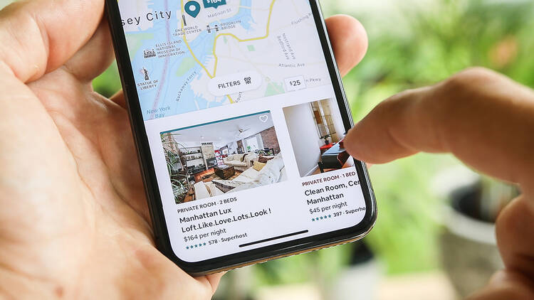 A person holds up a phone while looking at AirBnb rentals.