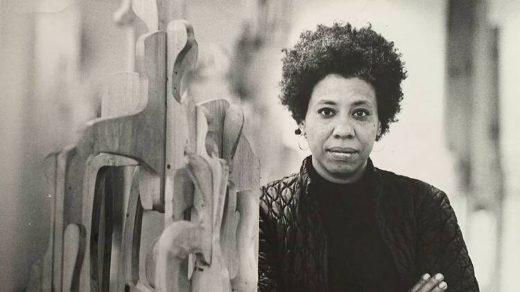 A portrait of a woman standing next to a sculpture.