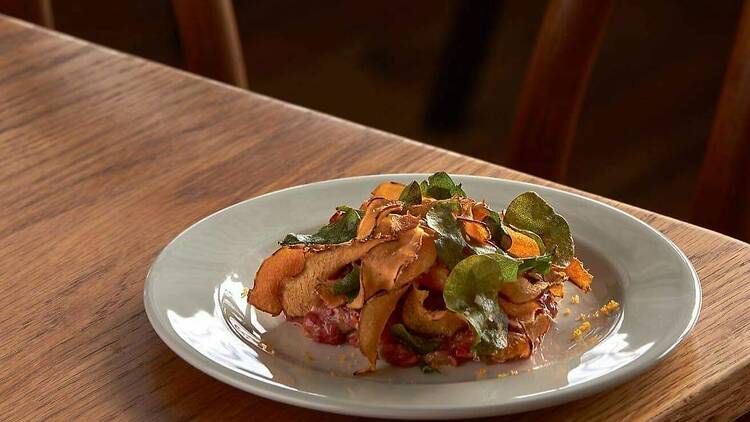 Tartare dish topped with crisp vegetables on a wooden table.