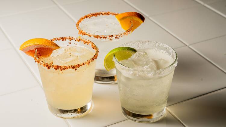 Three Mexican cocktails with salted rims and citrus wedges. 