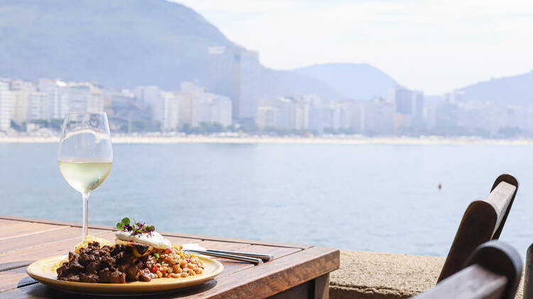 Prato de picadinho servido à mesa do Café 18 do Forte com vista para a orla de Copacabana