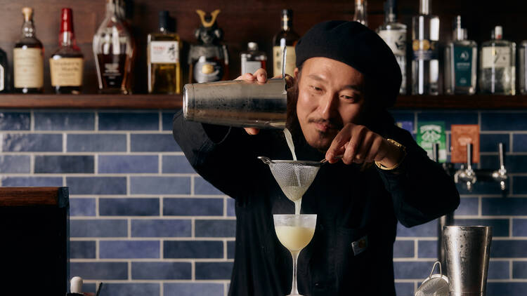 A bartender pours a cocktail into a glass through a strainer.