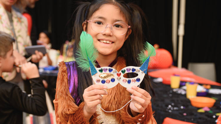 A girl holds up a mask she made at a Halloween party.