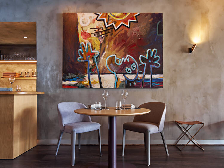 Dining table and chairs in front of a modern artwork at Amaru.