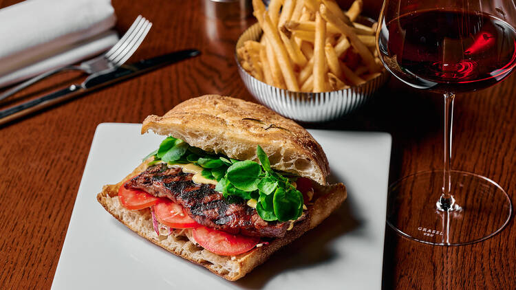 Steak sandwich, glass of red wine and fries.