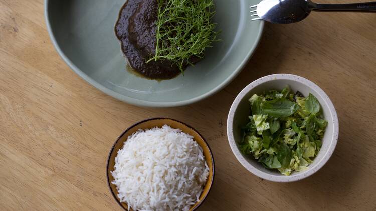 Plate of herb-garnished pork neck with bowls of rice and salad.