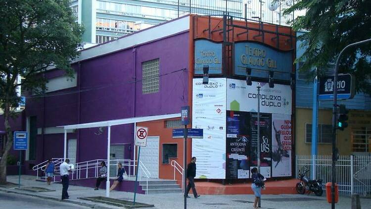 Esquina onde está o Teatro Glaucio Gill, com paredes pintadas de roxo de um lado e banners das peças em cartaz do outro