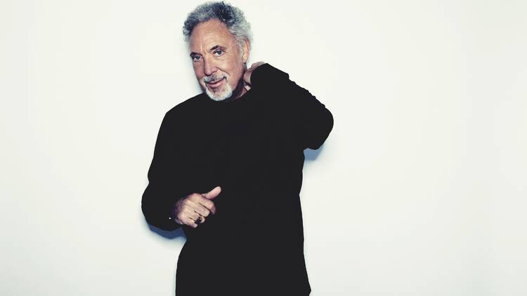 Singer Tom Jones dressed in black standing against a white backdrop.