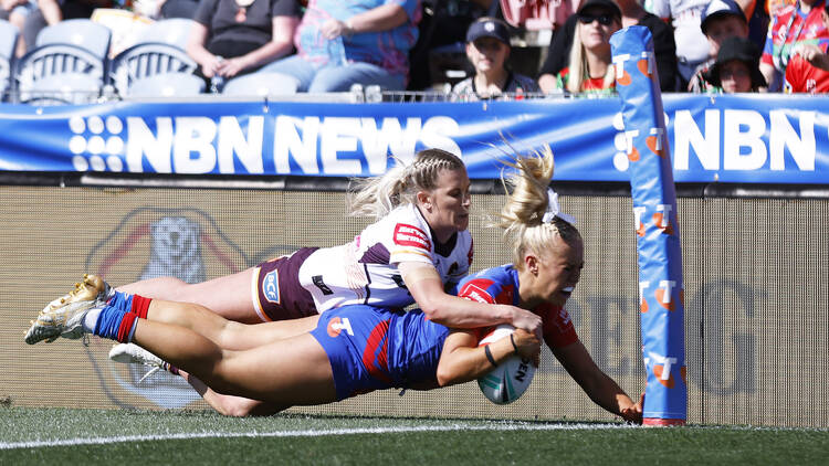 A female footballer tackling another female footballer scoring a try.